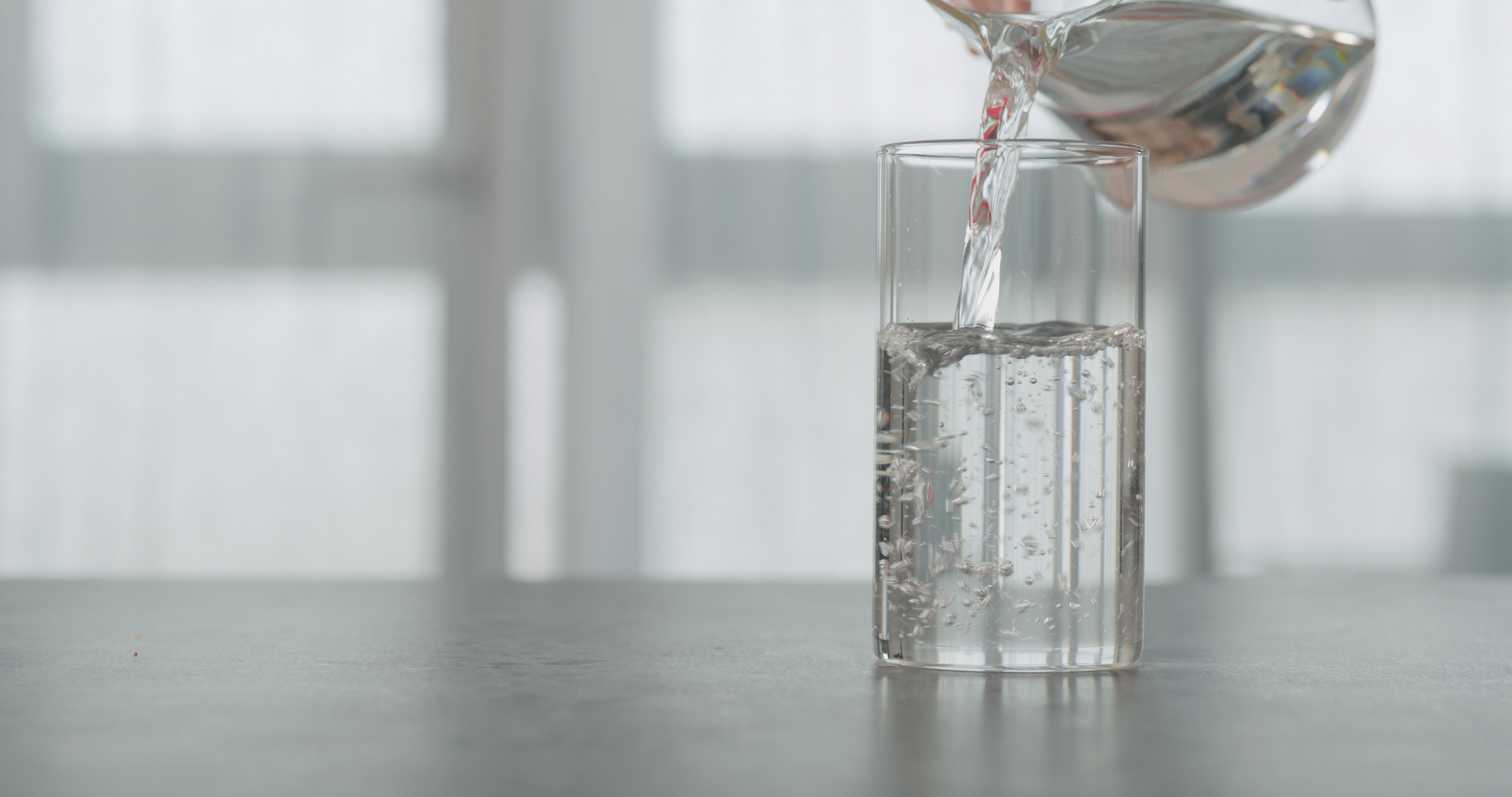 slow-motion-pour-water-in-beaker-glass-on-concrete-countertop-with-window-on-a-background_6144-x-3240-px