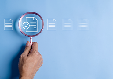 Hand holding a magnifying glass over a document icon with a checkmark, highlighting the review and approval process, symbolizing MDS Consulting’s commitment to excellence in technical documentation