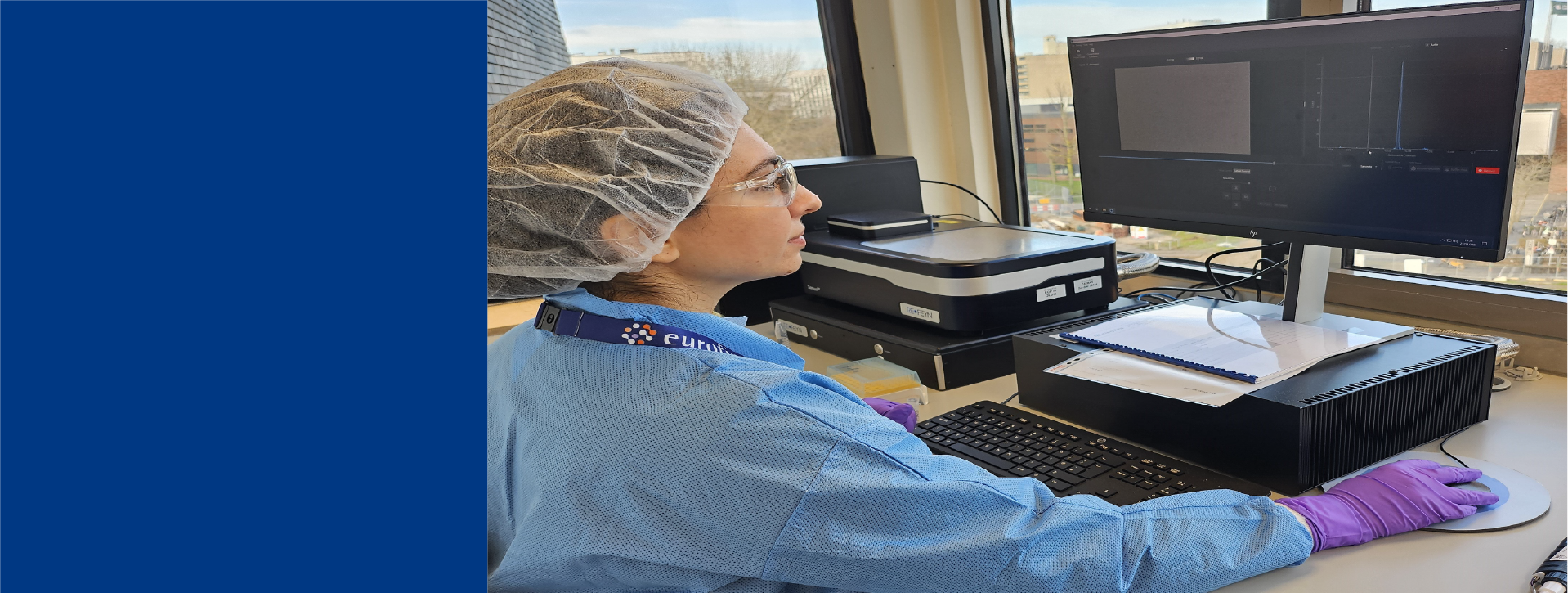 Lab technician in blue lab coat and gloves working on a computer with mass photometry equipment to analyze empty and full capsids.