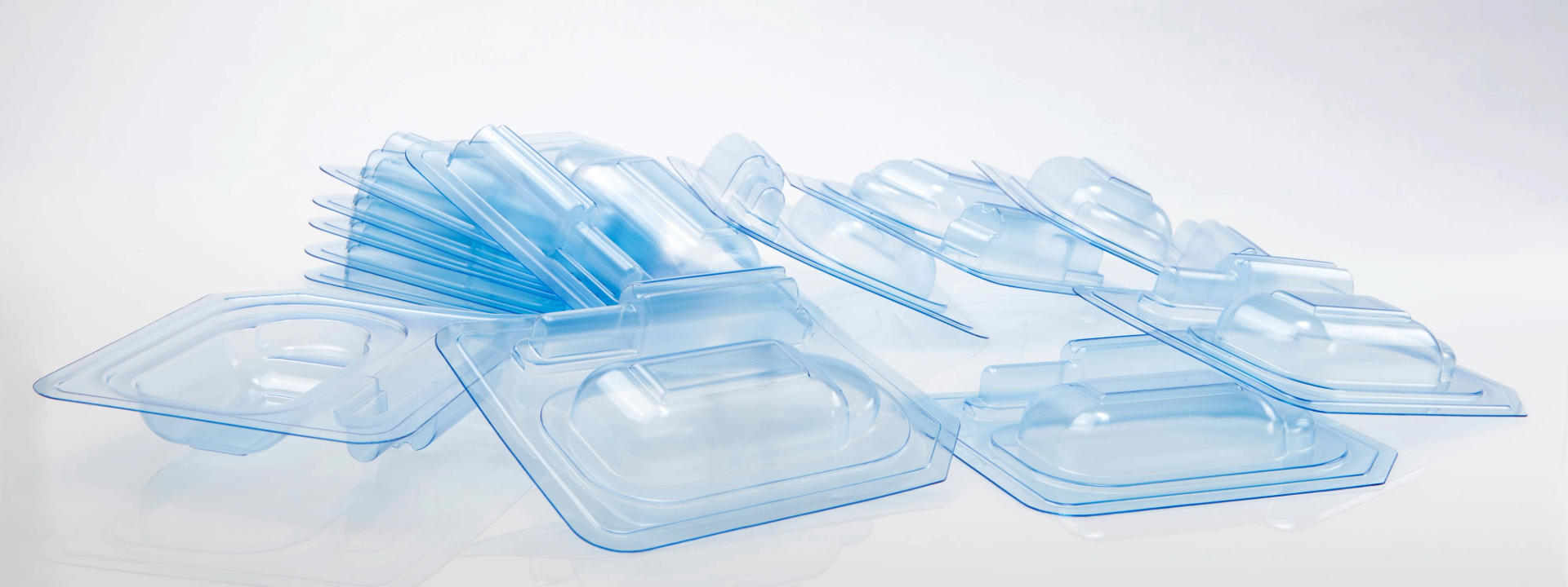 Gestapelte und überlappende transparente Blisterverpackungsschalen mit blauer Tönung, zur Aufbewahrung medizinischer Komponenten.