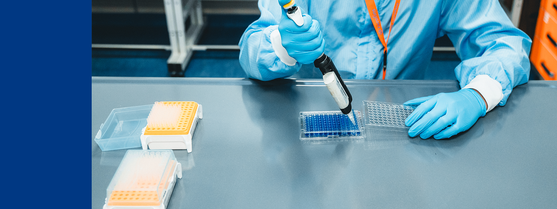 Mitarbeiter in vollständiger Schutzkleidung arbeitet mit einer Pipette an einer Petrischale in einem Labor.