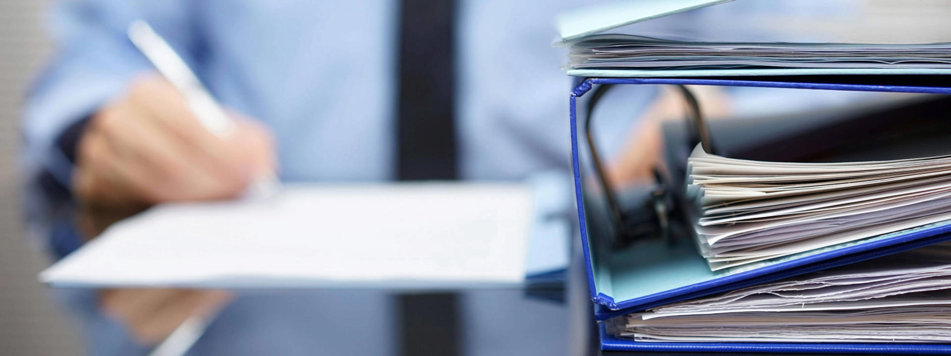 binders-with-papers-are-waiting-to-be-processed-with-businessman-back-in-blur-xl_9000x6000px1 (1)