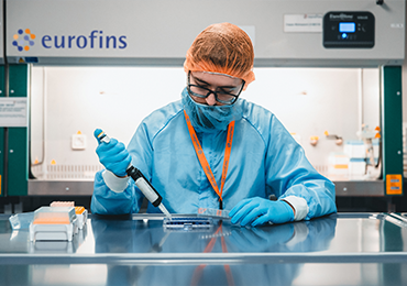 Mitarbeiter in vollständiger Schutzkleidung arbeitet mit einer Pipette an einer Petrischale in einem Labor.