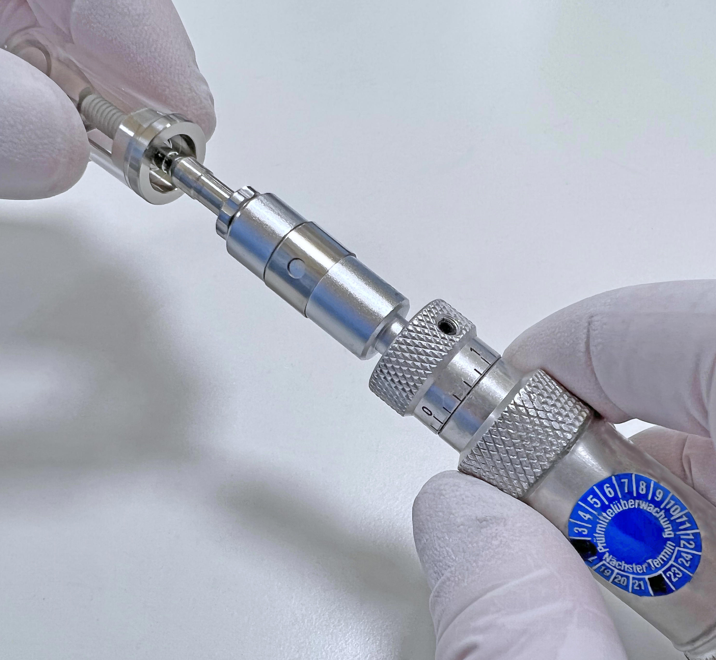 Eine behandschuhte Hand montiert ein Dentalimplantat mit metallischen Komponenten und einem blauen Ziffernring.