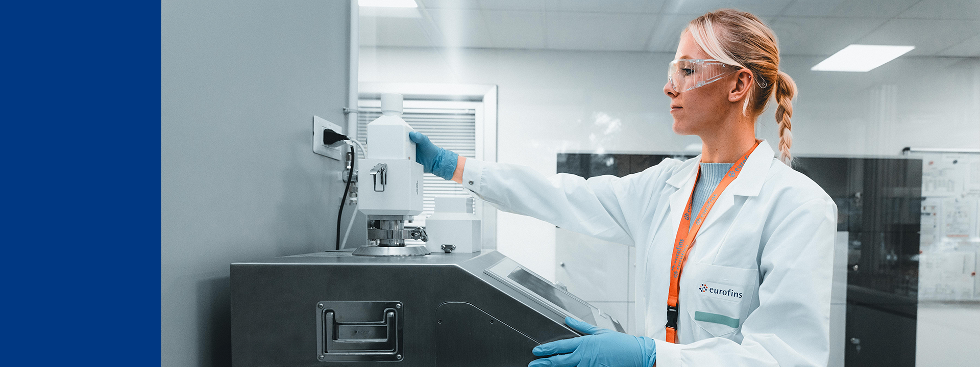 Laborfachkraft mit Schutzbrille und Handschuhen bedient ein Analysegerät in einem Labor.