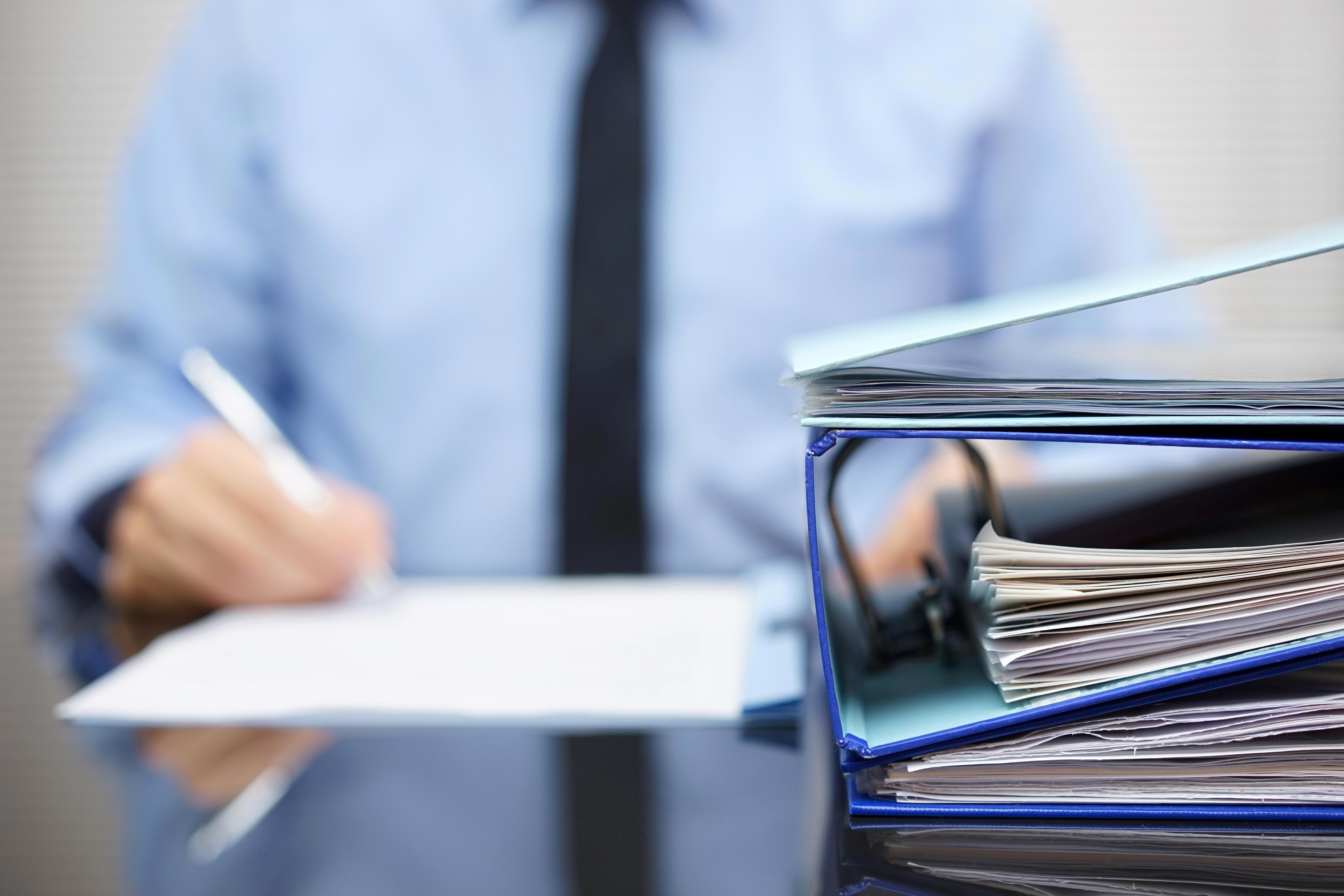 binders-with-papers-are-waiting-to-be-processed-with-businessman-back-in-blur-xl_9000x6000px