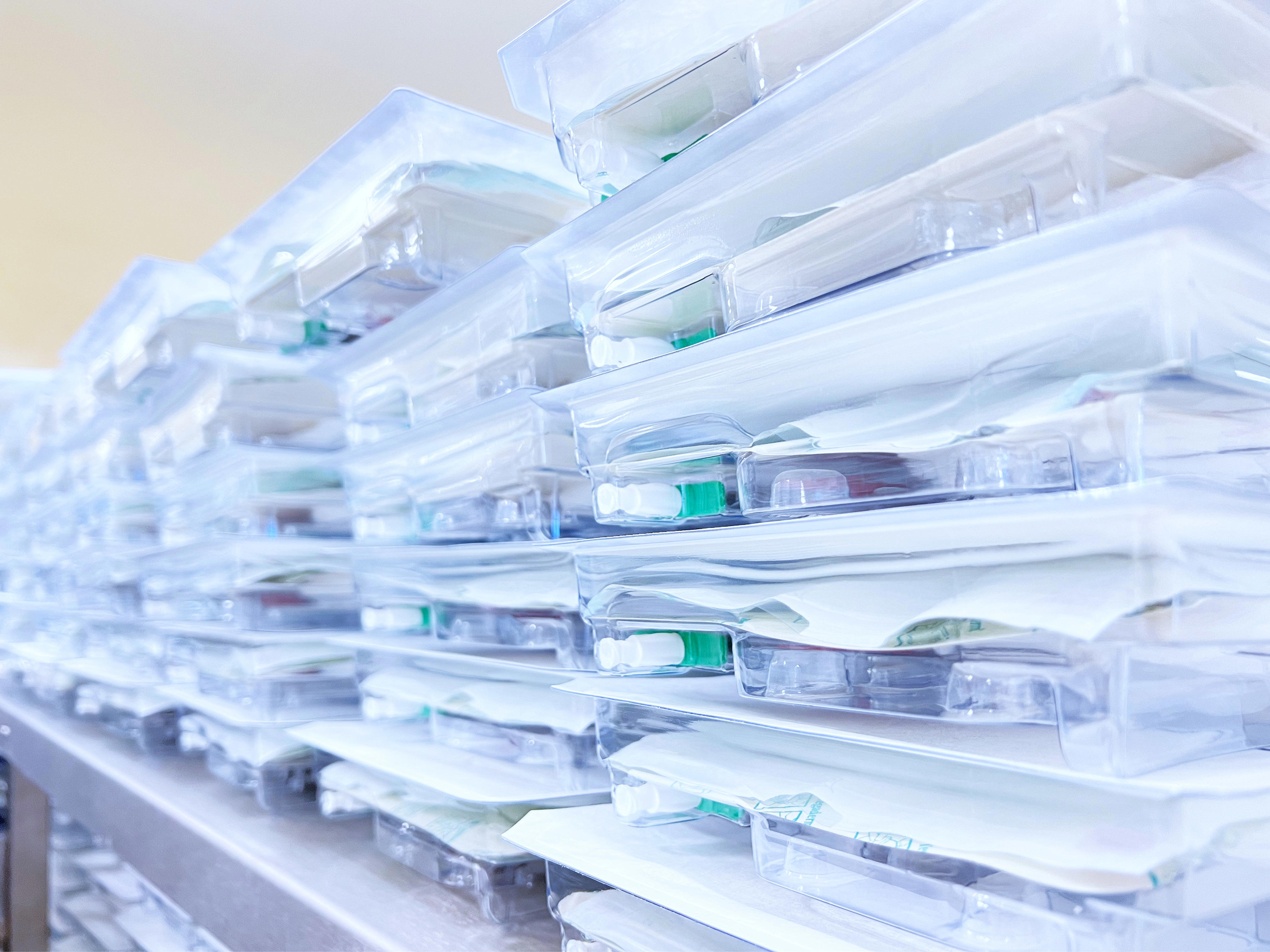 Ordentlich gestapelte Blisterverpackungen aus transparentem Kunststoff mit verschiedenen Komponenten auf einer Metalloberfläche.