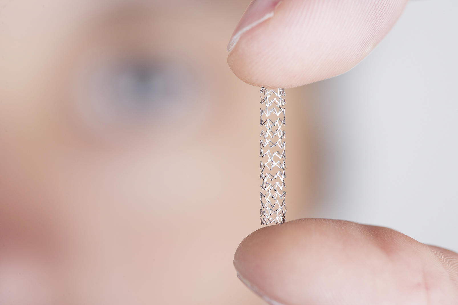 Nahaufnahme eines kleinen, zylindrischen medizinischen Stents mit feiner Netzstruktur, der zwischen zwei Fingern gehalten wird. 