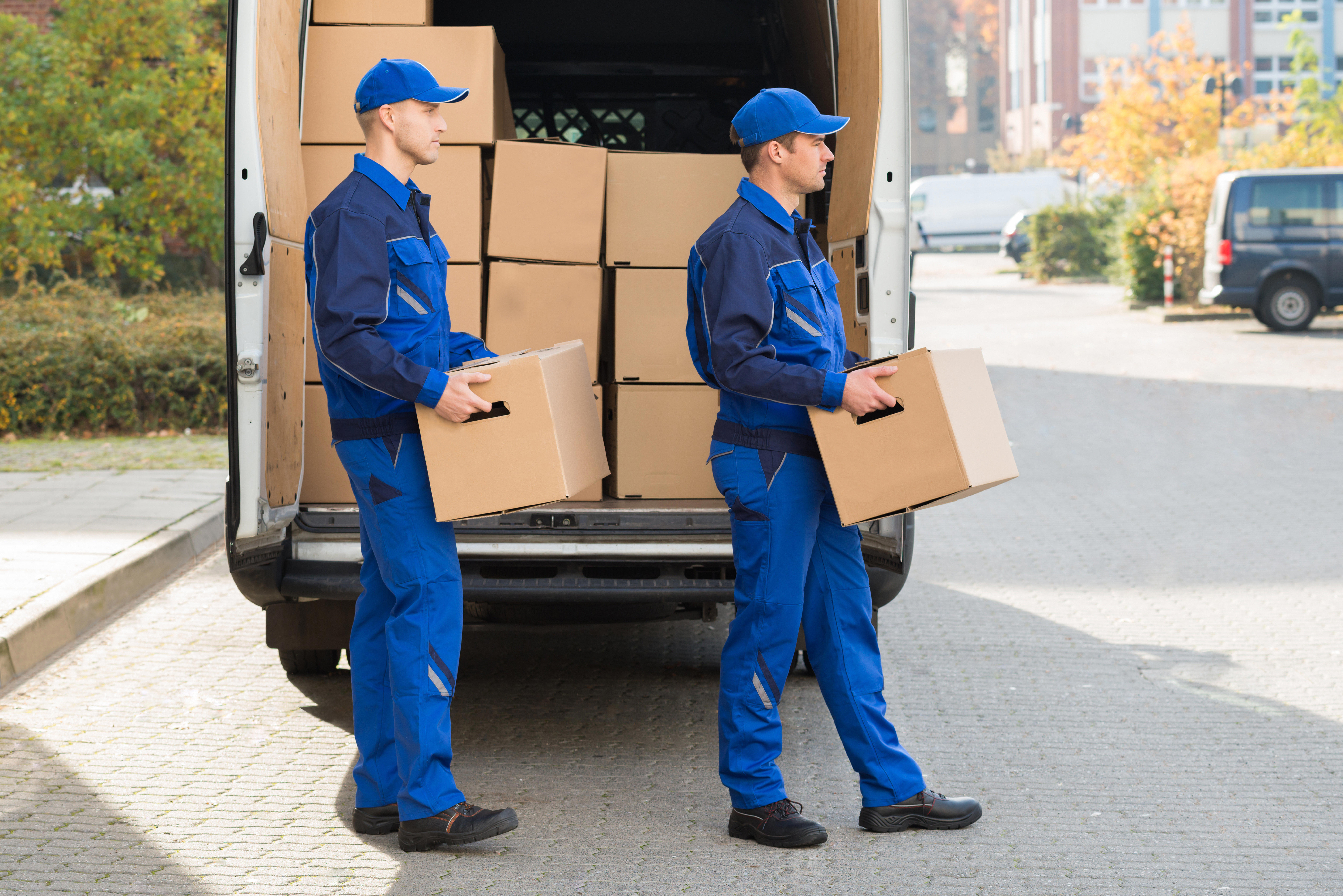 smiling-young-delivery-men-carrying-cardboard-boxes-while-walking-outside-truck_8211-x-5479-px