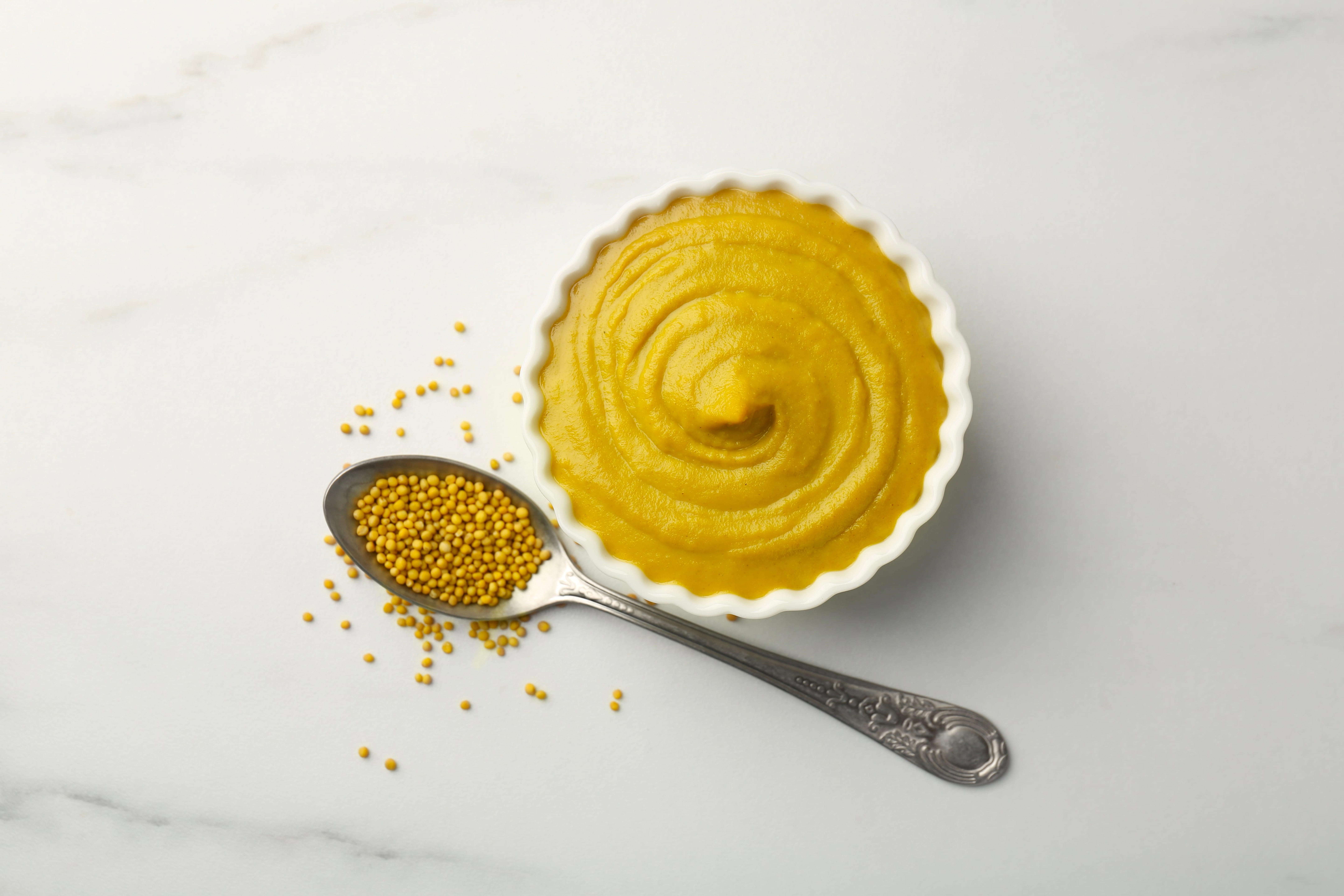 tasty-mustard-sauce-in-bowl-and-spoon-with-dry-seeds-on-white-marble-table-flat-lay_8640-x-5760px