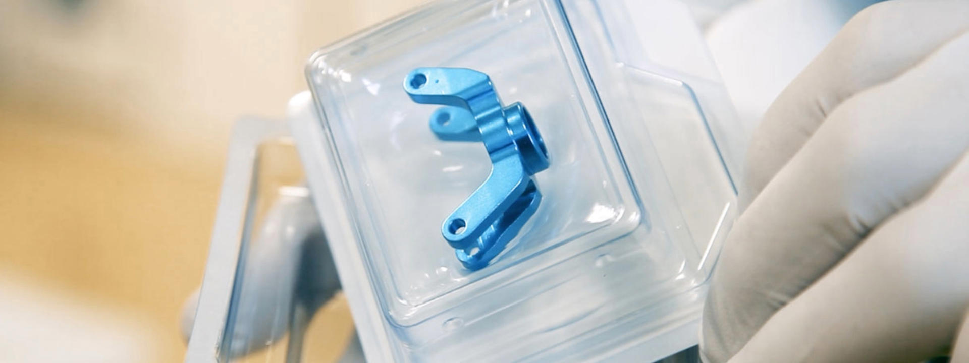 Blaues metallisches Medizinprodukt mit zwei Armen, die jeweils am Ende eine Öffnung aufweisen, in einer versiegelten Blisterverpackung.