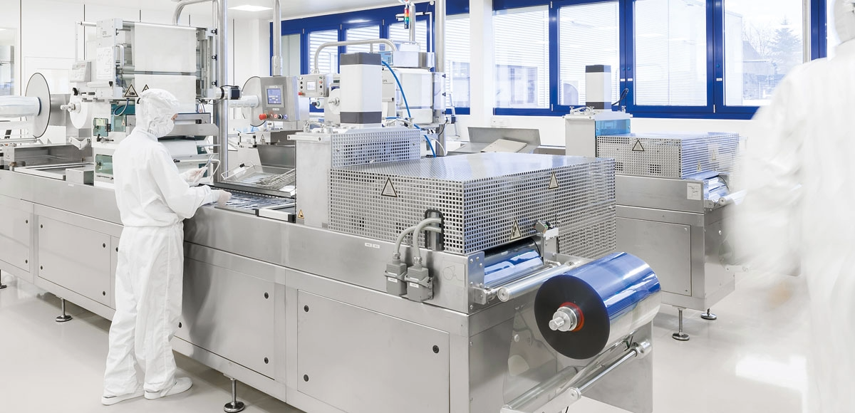 Produktionsmaschine zur Herstellung steriler Blisterverpackungen, im Hintergrund Personal in Reinraumkleidung.