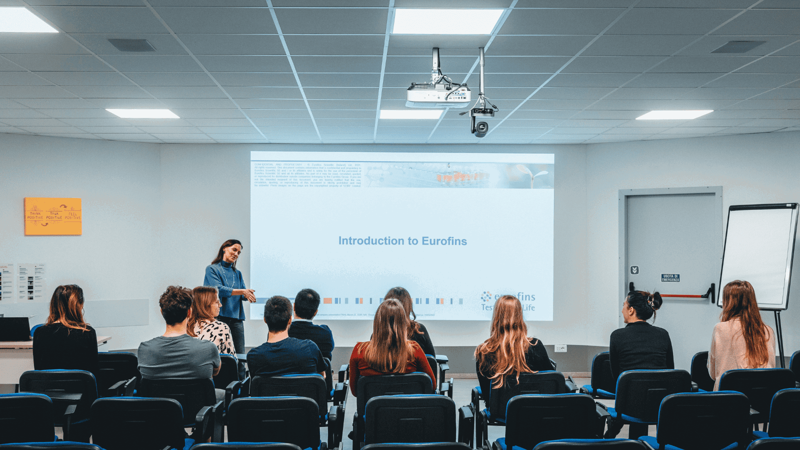 Ein Seminarraum mit mehreren Teilnehmenden, die einem Vortrag mit dem Titel „Introduction to Eurofins“ folgen. Die Referentin steht am Rednerpult vor einer großen Leinwand, moderne Ausstattung und ein Whiteboard sind im Raum sichtbar. 