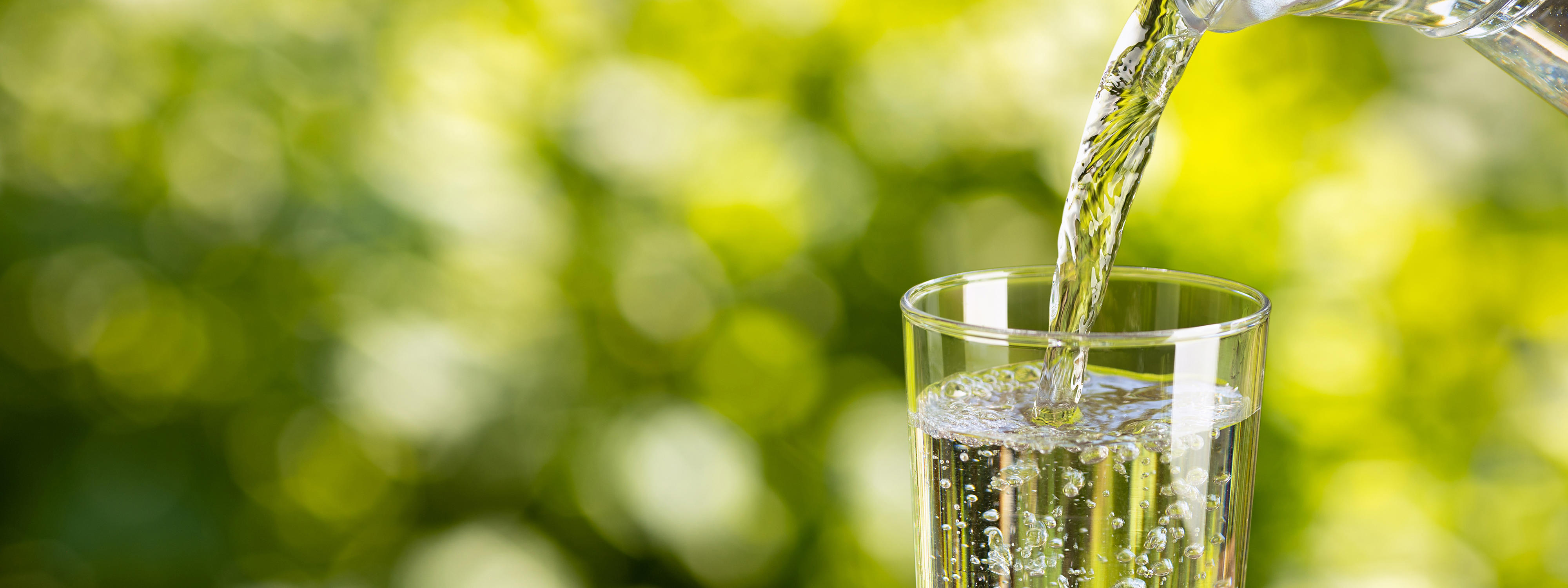 water-from-jug-pouring-into-glass-on-table-outdoors_1920x-720px
