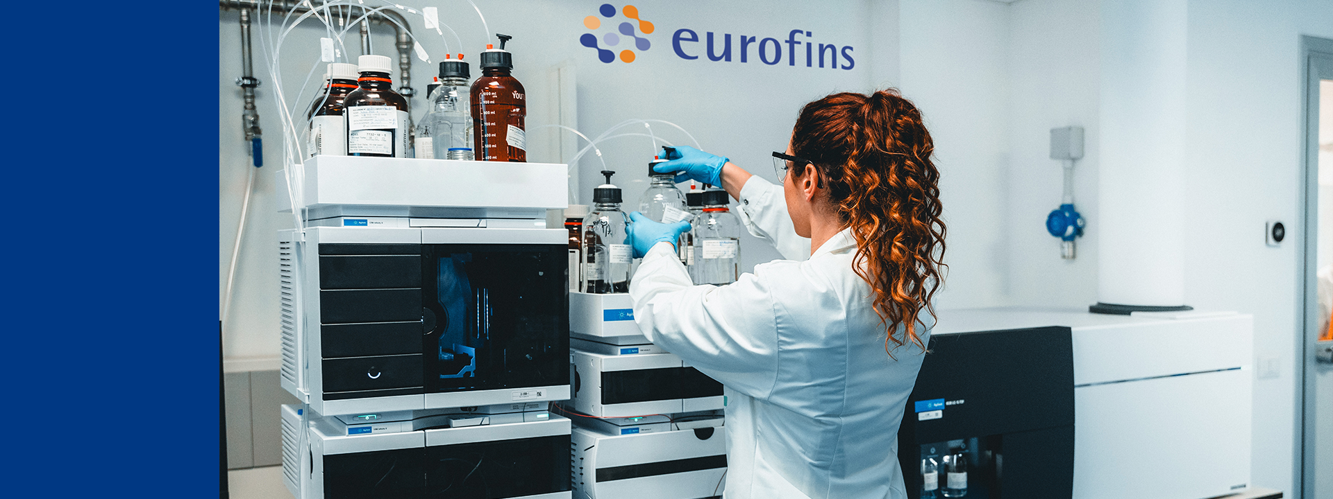 Mitarbeiterin im Laborkittel und mit Handschuhen arbeitet mit wissenschaftlichen Geräten und Flüssigkeitsbehältern in einem Eurofins-Labor.