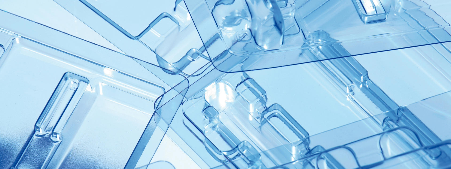 Nahaufnahme einer transparenten Kunststoffverpackung mit mehreren Fächern und komplexen Formen, mit blauer Tönung durch Beleuchtung oder Hintergrund.