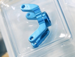 Blaues metallisches Medizinprodukt mit zwei Armen, die jeweils am Ende eine Öffnung aufweisen, in einer versiegelten Blisterverpackung. 