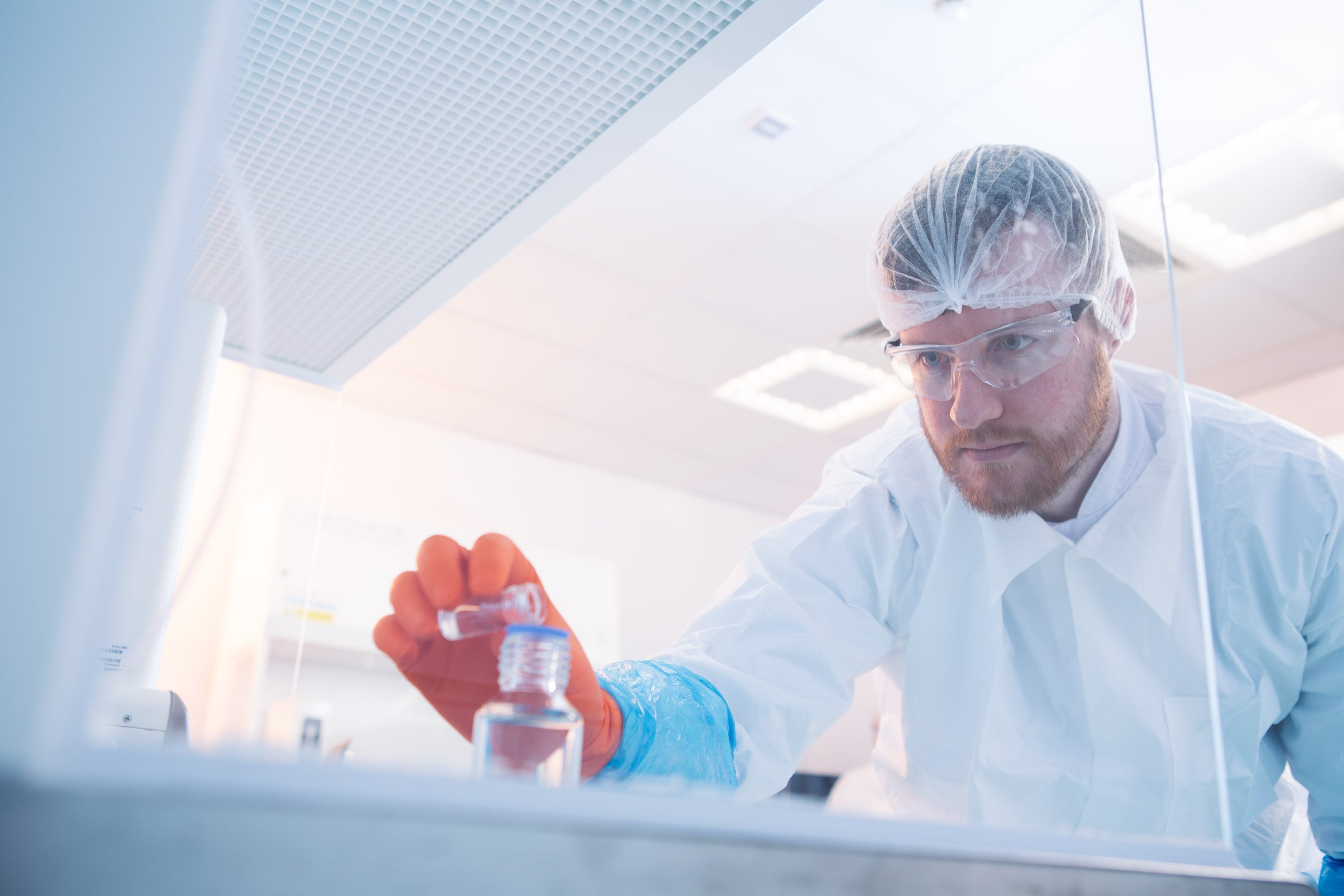 Scientifique en environnement stérile manipulant un flacon de liquide transparent, illustrant les méthodes de détection des endotoxines, y compris les tests pyrogènes et les solutions recombinantes, dans le cadre des services analytiques spécialisés proposés par Eurofins BioPharma Product Testing pour garantir la sécurité des produits pharmaceutiques et biotechnologiques.