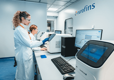 Laboratoire Eurofins BioPharma Product Testing spécialisé dans les tests de mycoplasmes : deux expertes de laboratoire certifié BPF travaillent sur des équipements numériques de haute technologie pour le contrôle qualité microbiologique. Le groupe Eurofins est reconnu pour ses services de biosécurité, de conformité réglementaire et de validation analytique dans le secteur pharmaceutique et biotechnologique.