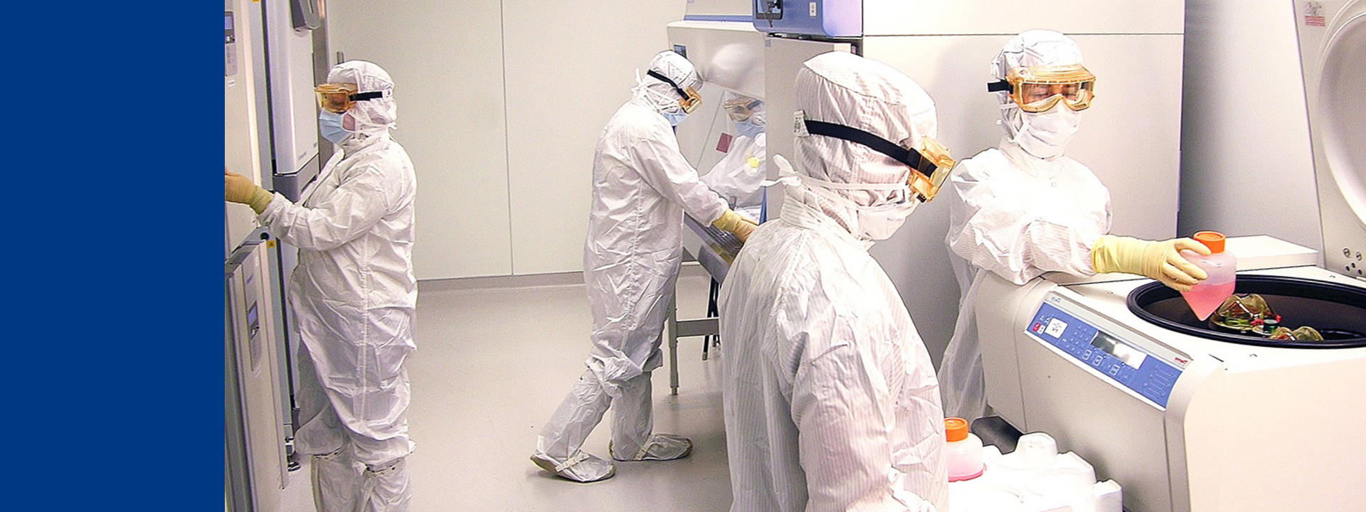 Activités de caractérisation de lignées cellulaires dans un laboratoire stérile Eurofins BioPharma Product Testing : des opérateurs en tenue de protection intégrale manipulent des équipements scientifiques, dont une centrifugeuse et des réfrigérateurs. L’image illustre les procédures critiques de contrôle qualité et de sécurité appliquées aux lignées cellulaires dans le développement de produits biopharmaceutiques, selon les bonnes pratiques de fabrication (BPF/GMP) et les exigences réglementaires.