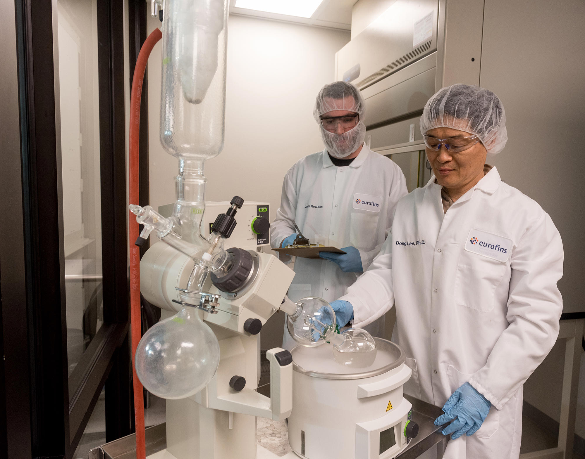 Techniciens de laboratoire chez Eurofins Biopharma Product Testing opérant un évaporateur rotatif dans le cadre de procédures de radiomarquage. Cette technique permet d’incorporer des isotopes radioactifs à des composés pharmaceutiques pour suivre leur comportement biologique. L’image illustre un environnement stérile et sécurisé dédié à la préparation, l’évaporation de solvants et le contrôle qualité des substances marquées, conformément aux normes BPF et aux exigences réglementaires.