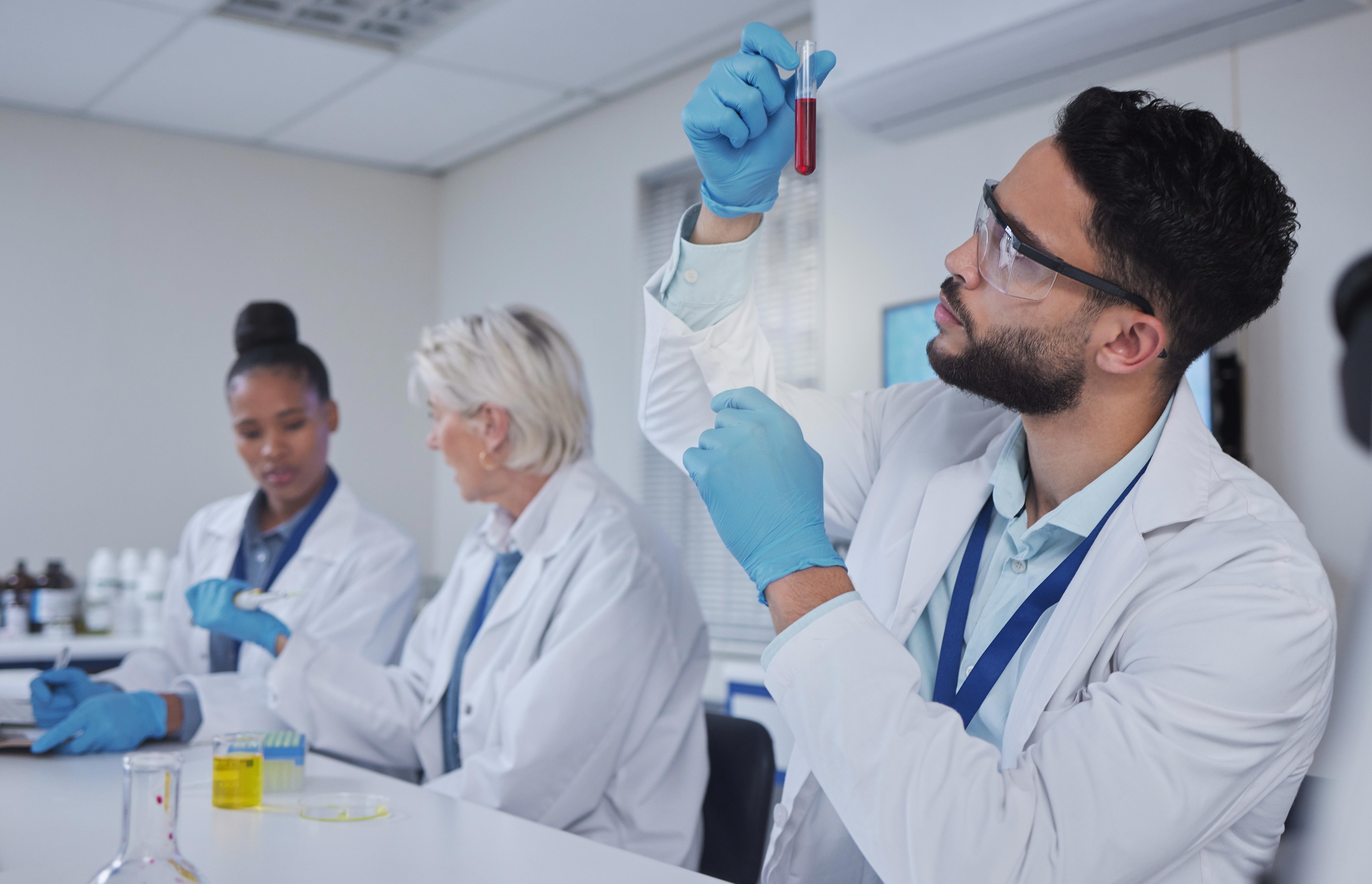 scientist-examining-a-blood-sample-in-a-laboratory-with-colleagues-in-background_-7533-x-4855-px