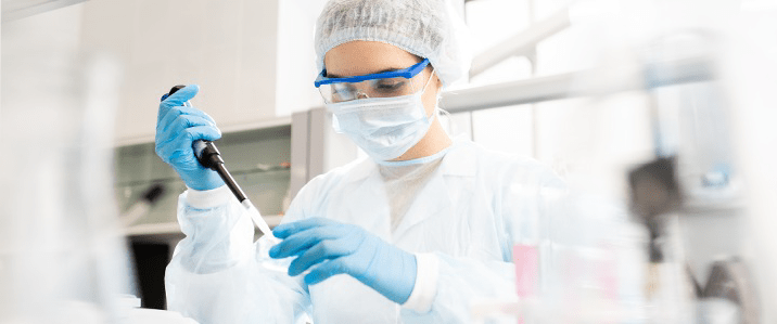 Technicien de laboratoire chez Eurofins BioPharma Product Testing, vêtu d’une blouse blanche, de gants bleus, d’un masque facial et de lunettes de protection, manipulant un liquide à l’aide d’une pipette dans un environnement contrôlé. Cette image illustre les pratiques conformes à la Pharmacopée Européenne 5.2.6, notamment les exigences liées à la manipulation aseptique, à la sécurité du personnel et à la précision des dosages dans le cadre du contrôle qualité pharmaceutique.