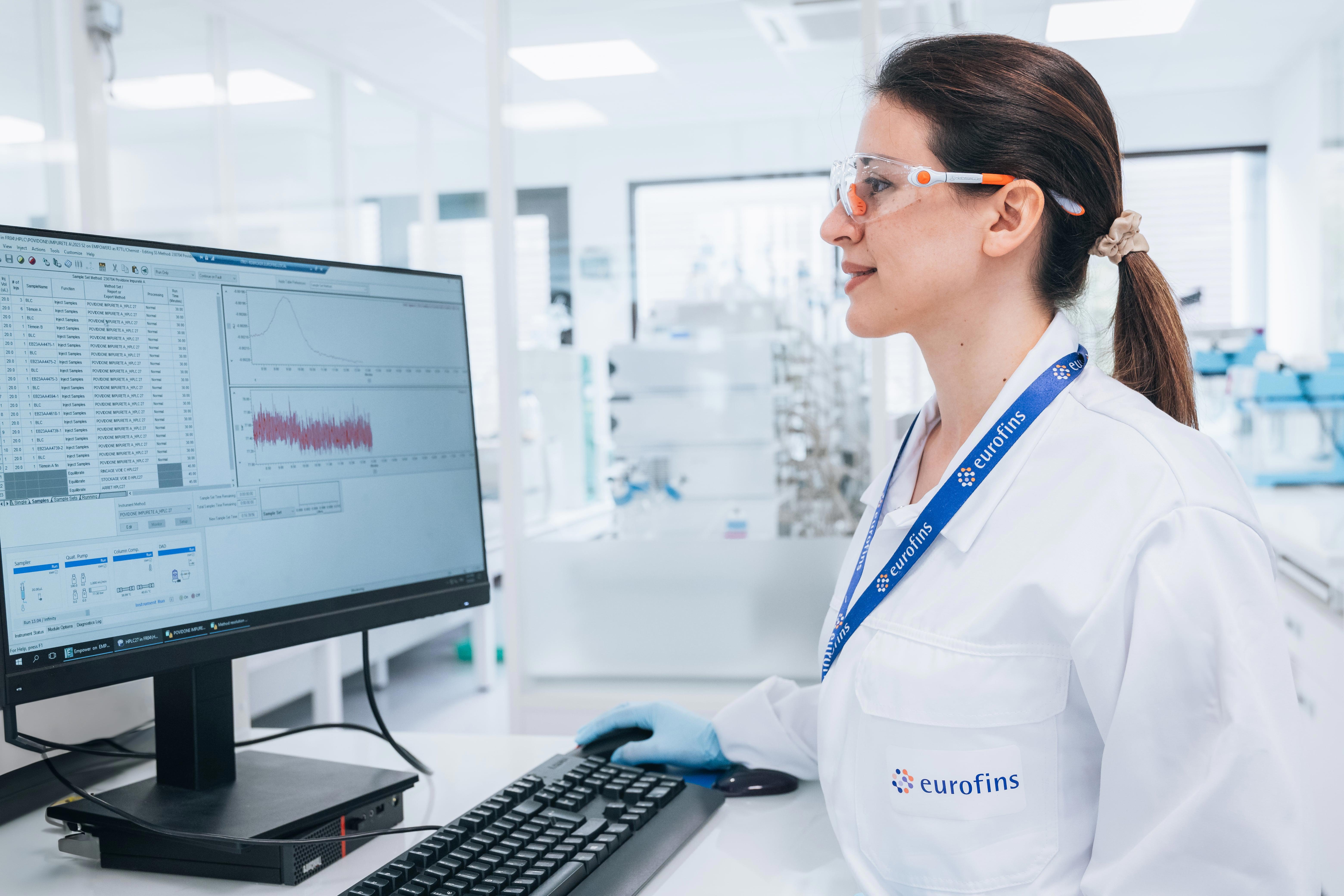 Collaborateur d’Eurofins BioPharma Product Testing travaillant sur un ordinateur dans un laboratoire moderne, portant une blouse avec le logo Eurofins et des lunettes de protection. L’écran affiche des données scientifiques et des graphiques, illustrant les activités de recherche et développement, l’analyse de données analytiques et les services de contrôle qualité pour l’industrie biopharmaceutique. En arrière-plan, équipements de laboratoire et environnement technique conforme aux normes de sécurité.