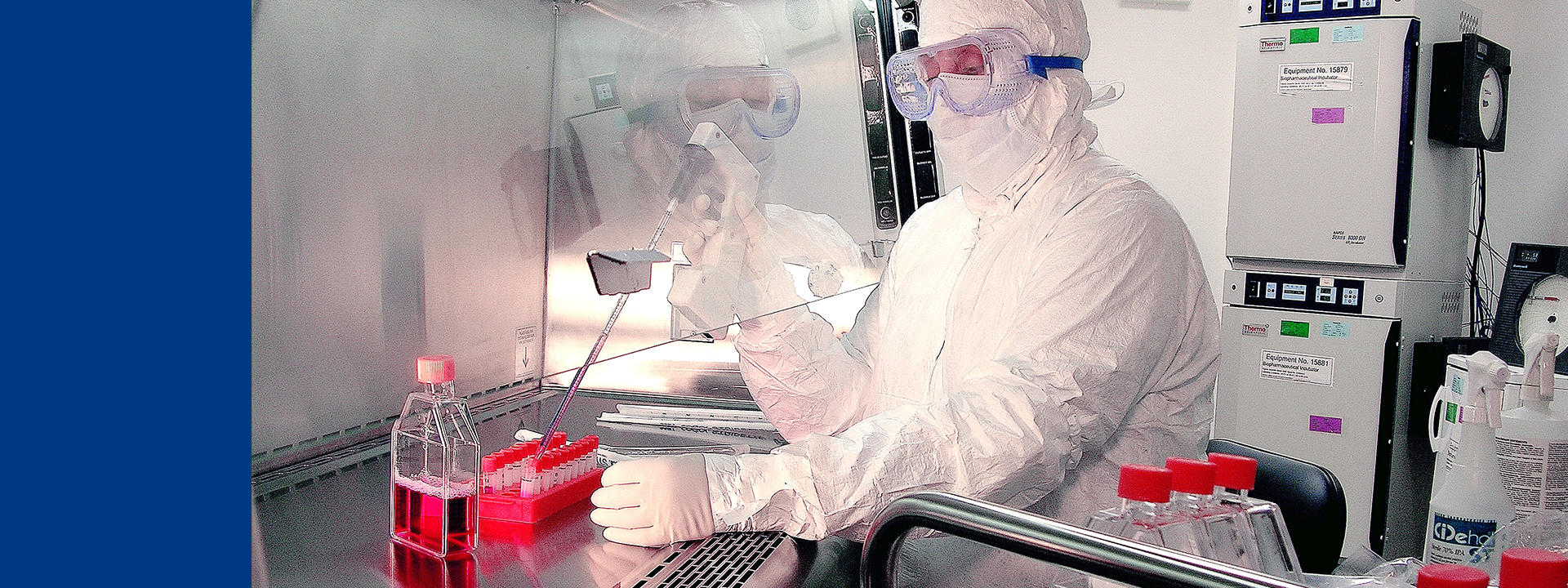 Procédure de cell banking dans un laboratoire stérile Eurofins BioPharma Product Testing : un opérateur en tenue de protection manipule des échantillons à la pipette sous hotte de biosécurité. Des flacons contenant des milieux de culture sont disposés sur la paillasse. Cette étape est essentielle pour la traçabilité et la conservation des lignées cellulaires utilisées dans le développement biopharmaceutique et la production de médicaments biologiques, selon les bonnes pratiques de fabrication (BPF/GMP).