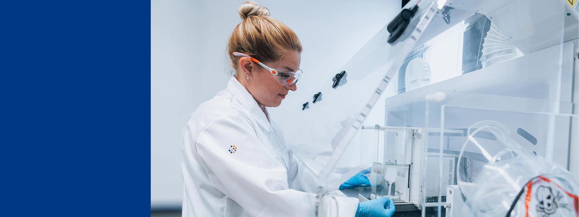 Technicienne de laboratoire Eurofins Biopharma Product Testing travaillant sous une hotte de sécurité, portant une blouse et des gants de protection. L’image montre un environnement stérile avec des équipements spécialisés pour la manipulation de substances hautement actives, incluant des dispositifs de confinement et des instruments analytiques.