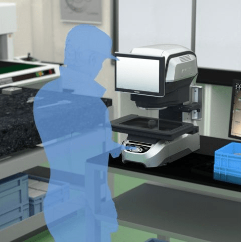 Poste de travail en laboratoire chez Eurofins BioPharma Product Testing, équipé d’un microscope numérique avec écran intégré et commandes de précision, utilisé pour les mesures dimensionnelles d’échantillons pharmaceutiques. Une silhouette bleue translucide indique la position de l’opérateur devant l’appareil. Le plan de travail comprend également des boîtes de rangement et du matériel complémentaire, illustrant un environnement organisé dédié à l’analyse métrologique et au contrôle qualité.