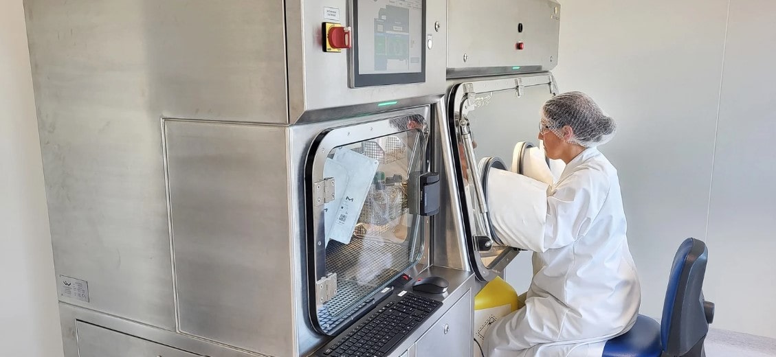 Technicienne de laboratoire en salle propre manipulant un isolateur pour réaliser un essai de stérilité, illustrant les protocoles aseptiques stricts appliqués par Eurofins BioPharma Product Testing dans le contrôle qualité des produits biologiques.