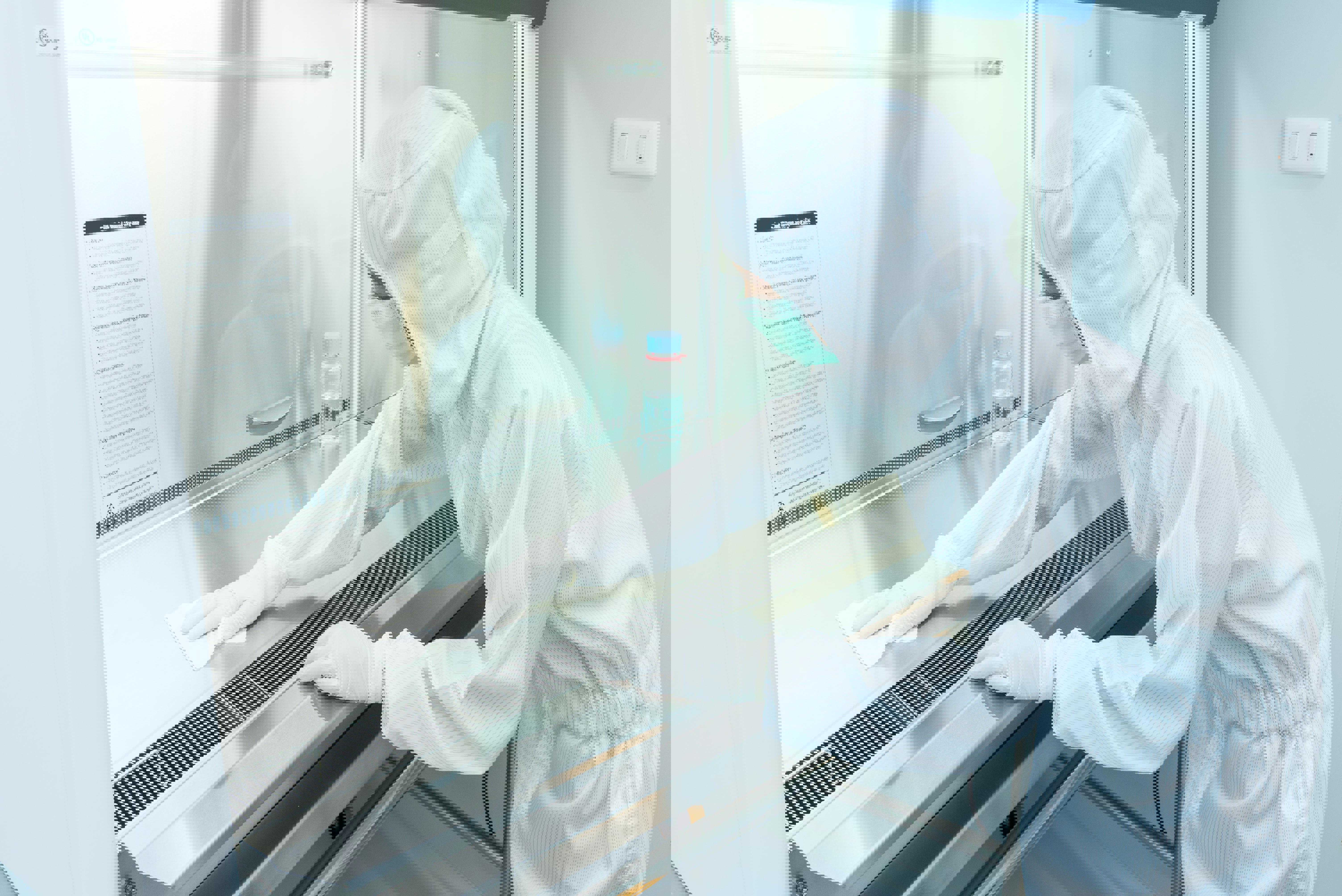 Technicien en salle propre chez Eurofins Biopharma Product Testing nettoyant une enceinte de sécurité microbiologique selon les exigences de l’annexe 1 des Bonnes Pratiques de Fabrication (BPF), garantissant un environnement aseptique pour les tests de stérilité.