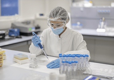 Technicien d’Eurofins BioPharma Product Testing réalisant une opération de monitoring environnemental en laboratoire pharmaceutique. Équipé d’une blouse, d’un masque, d’une charlotte et de gants, il utilise une pipette pour transférer un liquide dans des tubes à essai. L’environnement de travail, conforme aux normes GMP, est équipé de matériel scientifique destiné au contrôle microbiologique et à la surveillance de la contamination particulaire et biologique.