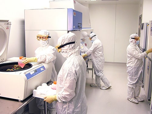 Procédure de cell banking dans un laboratoire stérile Eurofins BioPharma Product Testing : des techniciens en EPI complets manipulent une centrifugeuse et des équipements de bioproduction. Cette étape essentielle du développement biopharmaceutique garantit la traçabilité, la sécurité et la conservation des lignées cellulaires utilisées dans les tests de conformité réglementaire et les études de stabilité.