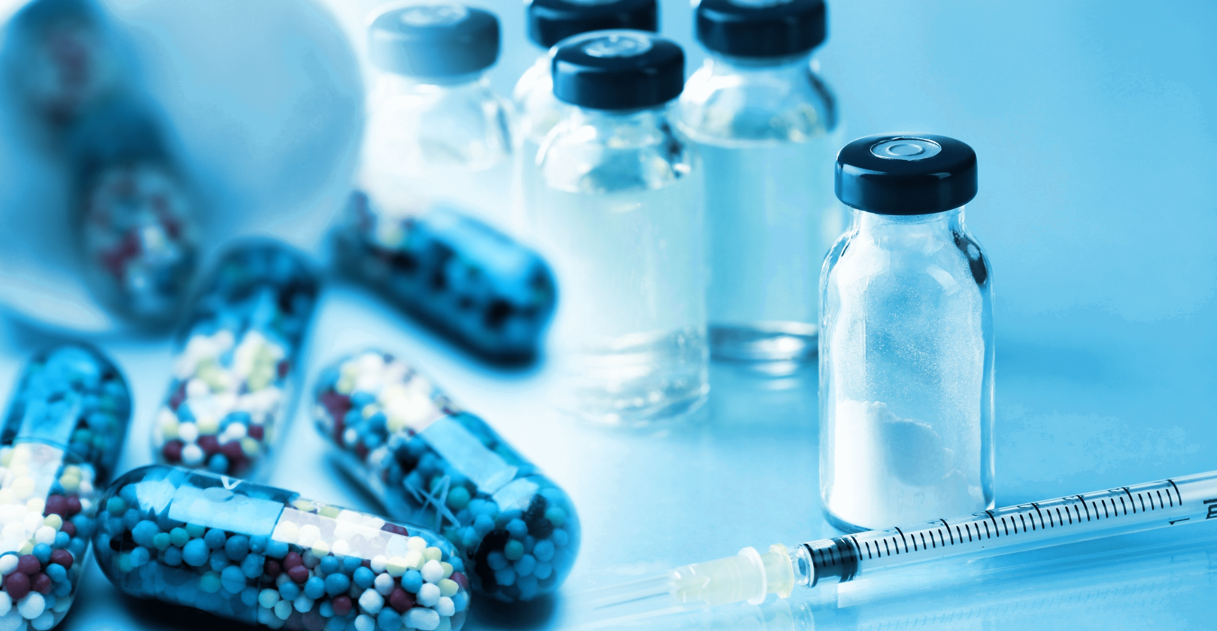 Image illustrant les tests de conditionnement réalisés chez Eurofins BioPharma Product Testing : plusieurs flacons en verre contenant un liquide clair, munis de bouchons noirs, sont disposés sur une surface bleue. À gauche, des capsules remplies de billes colorées évoquent des formes galéniques innovantes, tandis qu’une seringue est placée au premier plan. Cette composition met en évidence les éléments utilisés pour évaluer la compatibilité, l’intégrité et la sécurité des emballages pharmaceutiques.