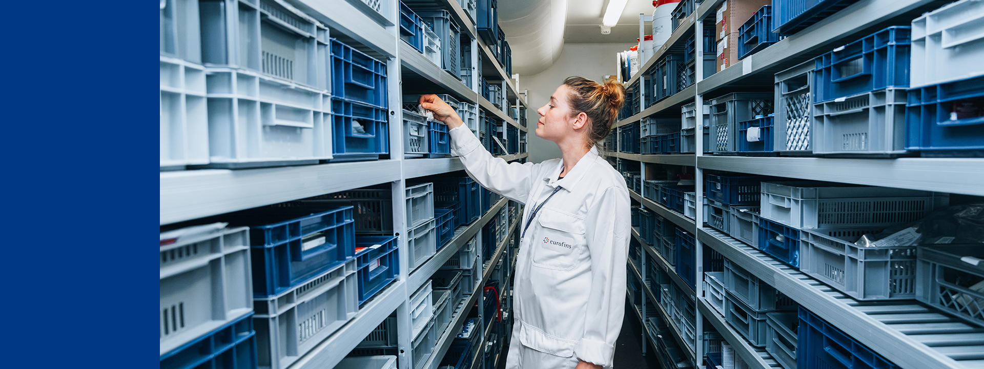 Technicienne de laboration Eurofins BioPharma Product Testing accédant à des bacs d’échantillons dans un espace de stockage en environnement contrôlé pour études de stabilité pharmaceutique, illustrant la gestion rigoureuse d’inventaire d’échantillons soumis aux conditions ICH (température, humidité, cycles accélérés) afin de déterminer la durée de conservation et garantir la qualité des médicaments.