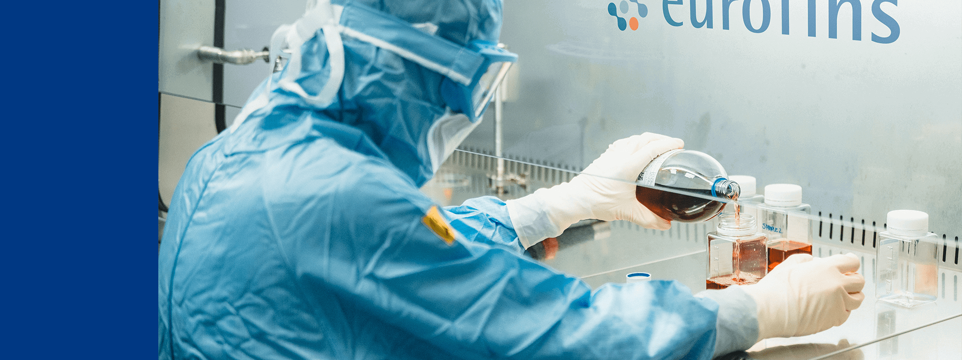Technicien de laboratoire en tenue stérile manipulant des solutions sous hotte à flux laminaire dans un laboratoire Eurofins BioPharma Product Testing, réalisant des tests de stérilité et analyses microbiologiques pour le contrôle qualité des produits pharmaceutiques. Équipement de protection complet incluant gants, masque et combinaison, garantissant la conformité aux normes GMP et ISO pour la sécurité des patients et la fiabilité des résultats.