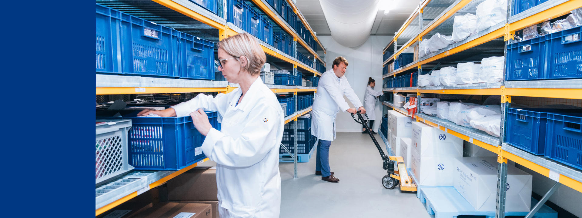 Zone de stockage pharmaceutique conforme aux BPF, avec étagères organisées, les technicens de laboratoire manipulent des bacs et équipements. Les capacités logistiques nécessaires aux études de stabilité incluent le contrôle des conditions de température, d’humidité et de traçabilité. Ce type d’installation garantit la sécurité des produits, la conformité réglementaire et l’efficacité des processus de stockage dans le cadre des essais de stabilité à long terme ou accélérés.