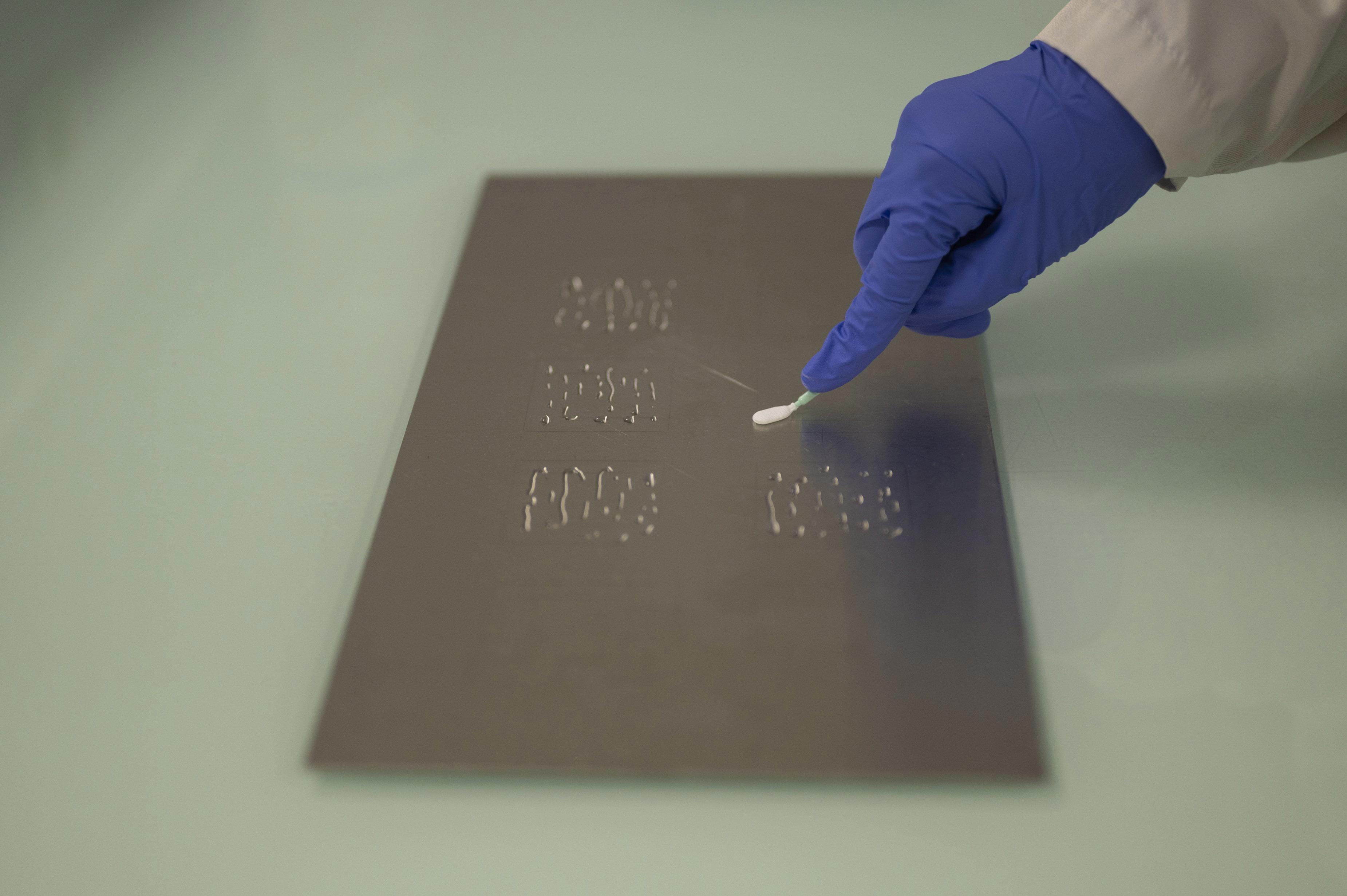 Technicien en laboratoire effectuant un prélèvement sur une surface métallique structurée à l’aide d’un coton-tige, illustrant les protocoles de validation du nettoyage adaptés aux différentes configurations d’équipements, tels que pratiqués par Eurofins BioPharma Product Testing.