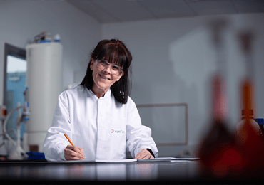 Laboratoire Eurofins BioPharma Product Testing dédié au développement et à la validation de méthodes pour les produits non répertoriés dans les pharmacopées. Une personne en blouse blanche prend des notes sur un document posé sur la paillasse. À l’avant-plan, des flacons et verreries de laboratoire sont visibles, tandis qu’en arrière-plan se trouvent des équipements analytiques, illustrant un environnement conforme aux normes de qualité et de précision.