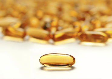 Gélule transparente de couleur ambrée en gros plan, mise en évidence au premier plan sur un fond flou composé de nombreuses autres gélules similaires. Cette image illustre les formes pharmaceutiques solides, telles que les compléments alimentaires ou les vitamines, dans le cadre des activités de contrôle qualité et de tests analytiques réalisés par Eurofins BioPharma Product Testing France, mettant en avant la précision des analyses et la traçabilité des produits finis.