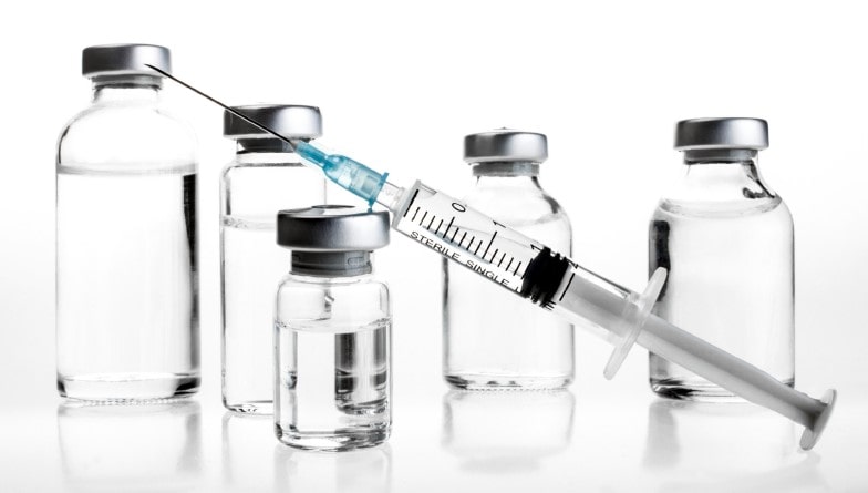 Cinq flacons en verre transparent contenant un liquide clair, avec bouchons métalliques, disposés sur fond blanc. Une seringue graduée, marquée "STERILE SINGLE USE", est insérée dans le bouchon du flacon central. Illustration utilisée par Eurofins BioPharma Product Testing pour représenter l’analyse de la stérilité et la conformité des systèmes plastiques d’emballage à usage pharmaceutique.