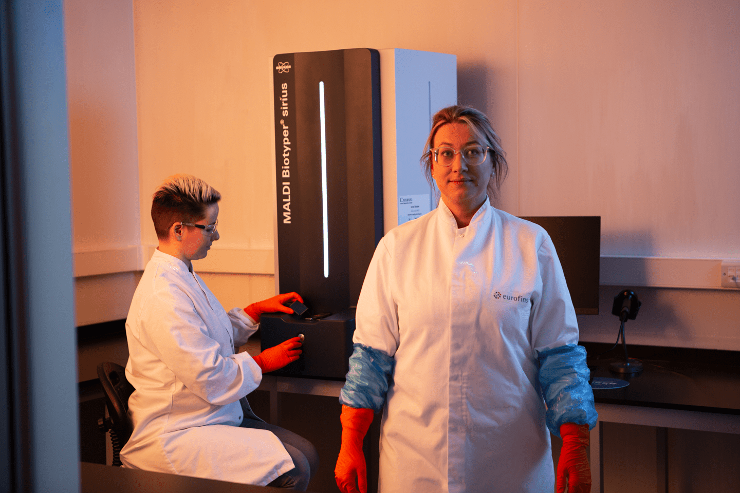 Deux techniciens de laboratoire Eurofins Biopharma Product Testing travaillant avec un système MALDI Biotyper Sirius pour l’identification microbienne. L’image montre un environnement de laboratoire équipé d’instruments analytiques, d’un ordinateur et de surfaces propres adaptées aux analyses pharmaceutiques.