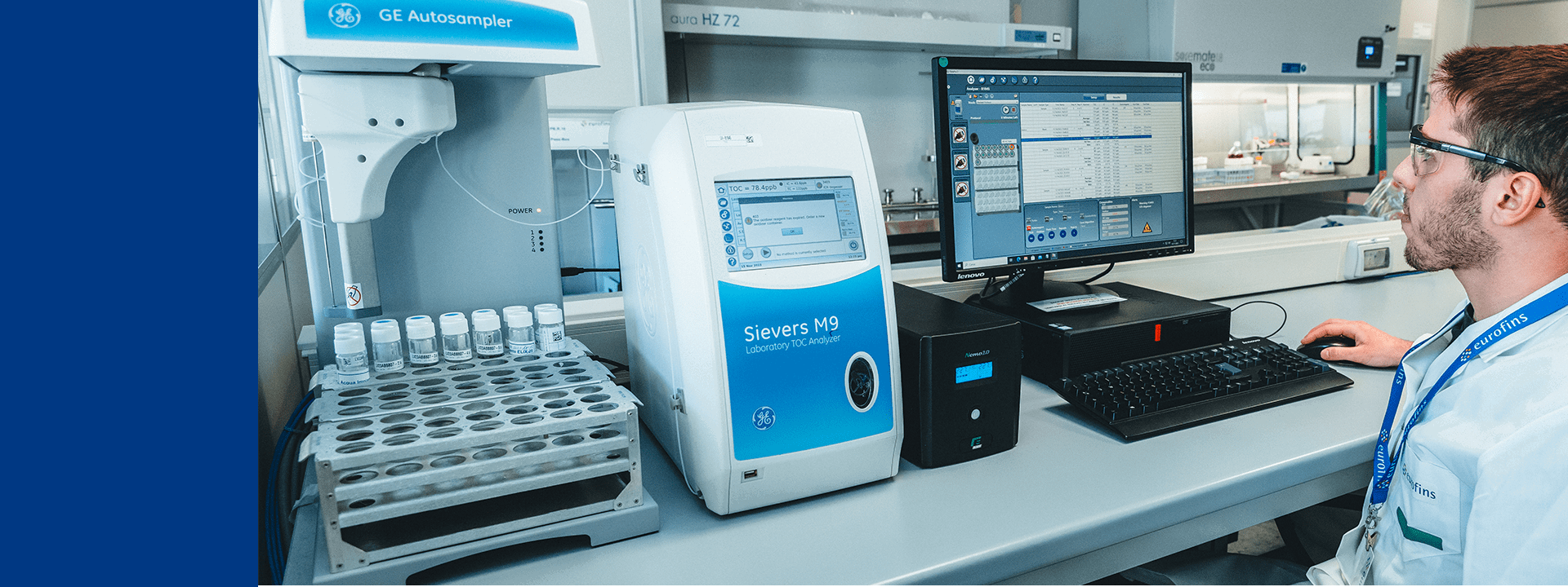 Un technicien Eurofins BioPharma Product Testing travaille sur un poste informatique relié à des équipements analytiques automatisés, dont un GE Autosampler et un analyseur TOC Sievers M9. Des échantillons sont disposées dans l’autosampler, tandis que l’écran du Sievers affiche des données en cours d’analyse. Il est équipé de lunettes de sécurité, interagit avec le logiciel de gestion des analyses, illustrant un environnement dédié au contrôle qualité des excipients, matières premières et principes actifs.