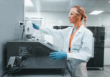 Un technicien de laboratoire d’Eurofins BioPharma Product Testing, vêtu d’une blouse blanche et de gants bleus, manipule une bouteille blanche devant un équipement analytique dans un environnement de laboratoire moderne et bien éclairé. Divers instruments scientifiques sont visibles en arrière-plan, illustrant les activités de contrôle qualité et de tests pharmaceutiques menés par Eurofins BPT France.