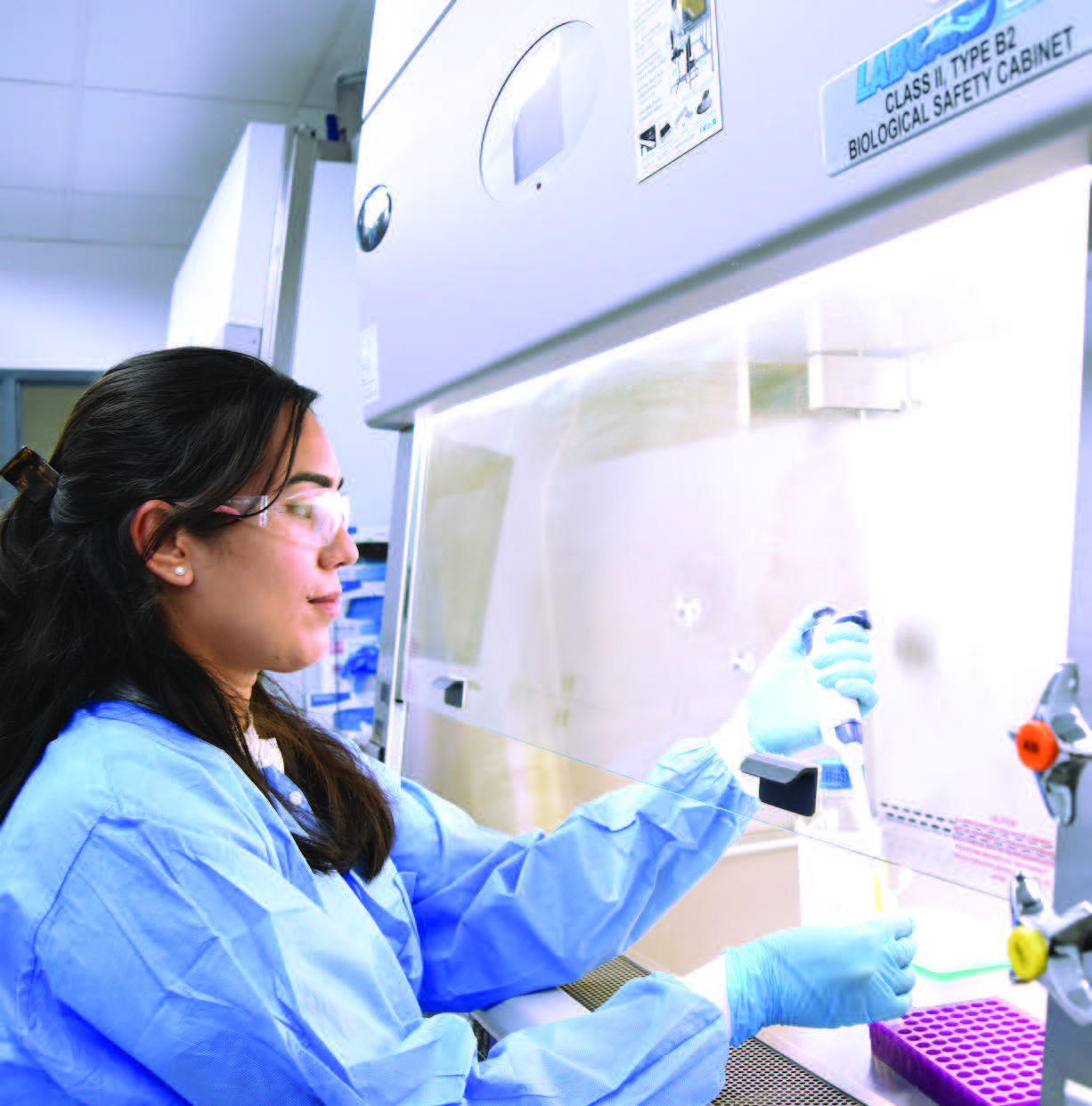 Technicienne de laboratoire Eurofins BioPharma Product Testing manipulant des échantillons sous hotte de sécurité biologique de classe II, équipé de blouse, gants et lunettes de protection, illustrant les protocoles de sécurité en laboratoire pour les tests pharmaceutiques et biologiques.