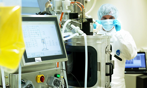 Installation de laboratoire pharmaceutique avec un grand bioréacteur en acier inoxydable, connecté à des capteurs et tubes, affichant des données techniques sur un écran numérique. Une personne en tenue stérile inspecte l’équipement en arrière-plan. Cette image illustre les technologies avancées utilisées par Eurofins BioPharma Product Testing pour les procédés de production et les analyses en environnement contrôlé.
