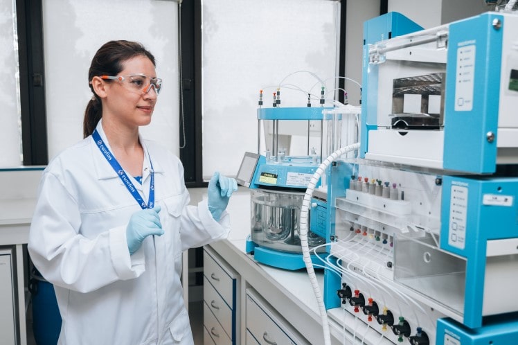 Scientifique en blouse de laboratoire et lunettes de protection opérant un équipement analytique complexe dans un environnement de laboratoire lumineux et organisé. Illustration utilisée par Eurofins BioPharma Product Testing pour représenter le développement, la validation et le contrôle qualité des essais de dissolution selon les normes pharmaceutiques.