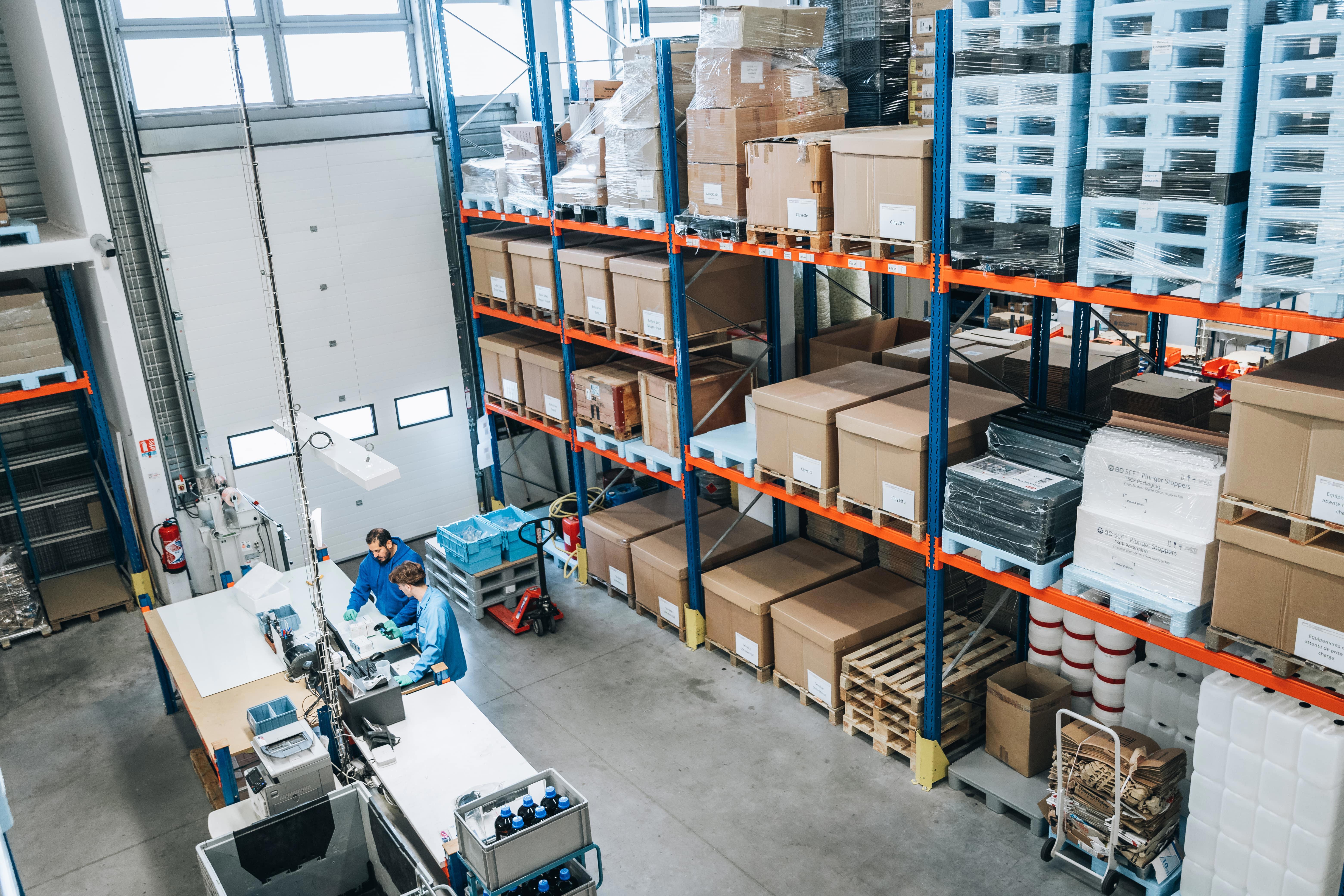 Entrepôt Eurofins BioPharma Product Testing : rayonnages métalliques chargés de cartons, personnel en activité, illustration de la gestion logistique et de la validation du plan de transport pour les études de stabilité.